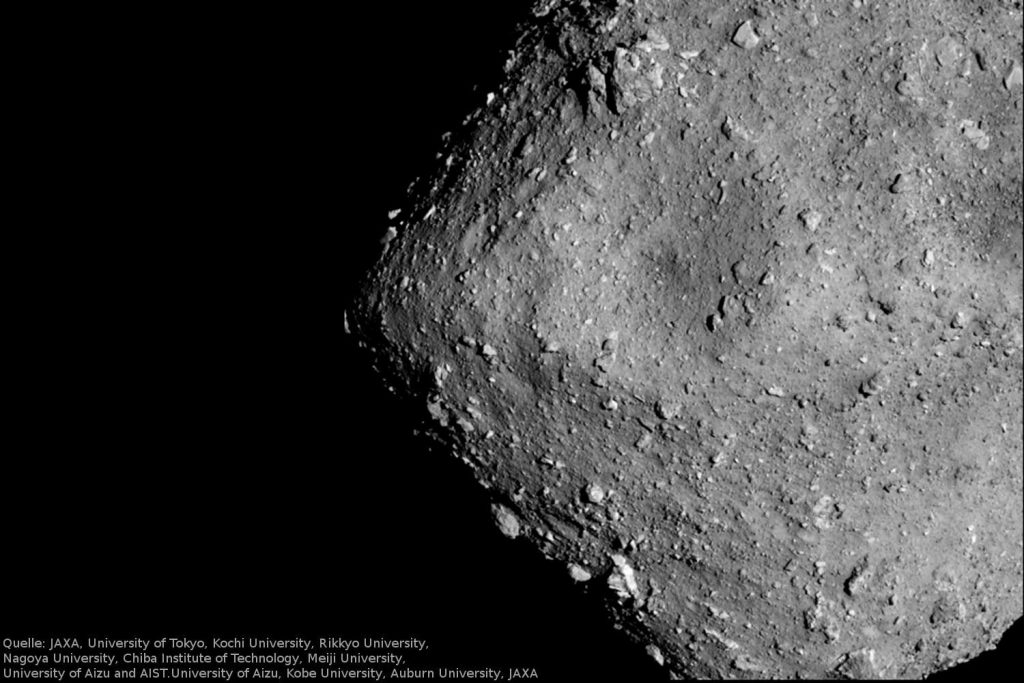 Dicht am Asteroiden Ryugu: Am 20. Juli 2018 nahm die optische Teleobjektivkamera (ONC-T) der japanischen Hayabusa2-Sonde den Asteroiden Ryugu aus sechs Kilometern Entfernung auf. Gut erkennbar sind die zahlreichen großen Felsbrocken auf der Asteroidenoberfläche sowie der große Krater in der Bildmitte. Ein Pixel entspricht etwa 60 Zentimetern.