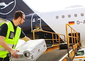 Loader places suitcases on the conveyor belt for loading a Lufthansa Airbus