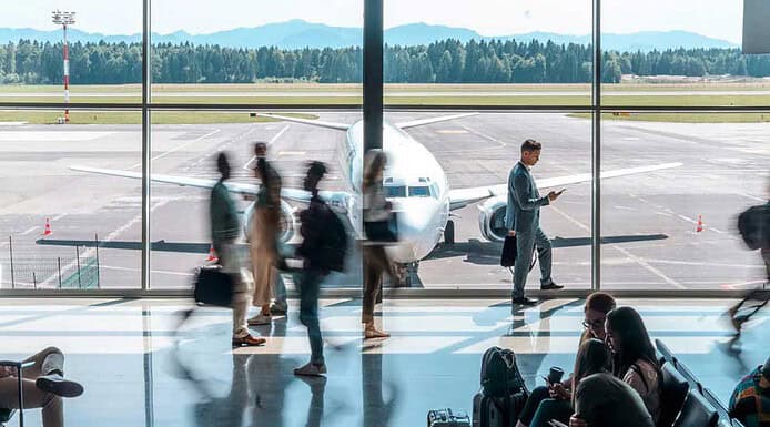Passagierabfertigung: SITA übernimmt Collins Aerospace Airport Solutions Passagiere am Flughafen warten auf ihren Flug, Blick auf das Flugzeug im Terminalfenster.